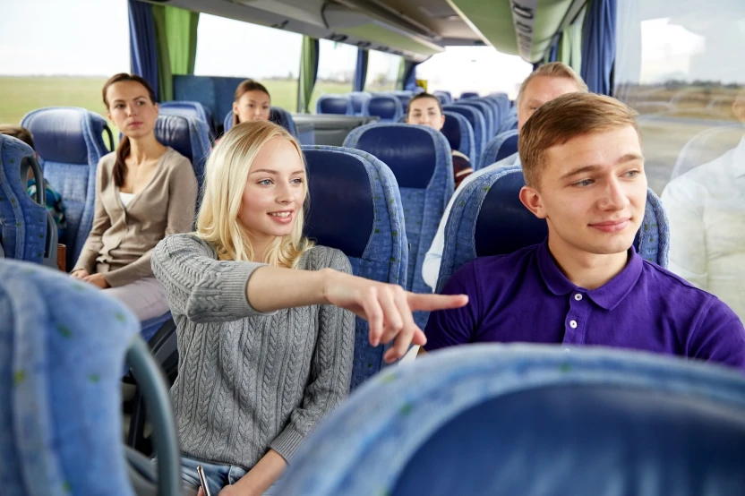 transport, tourism, road trip and people concept - young couple with group of tourists driving in travel bus and pointing finger to something outside