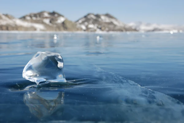 Transparent piece of ice on the mirrored surface of frozen lake. Low depth-in view.