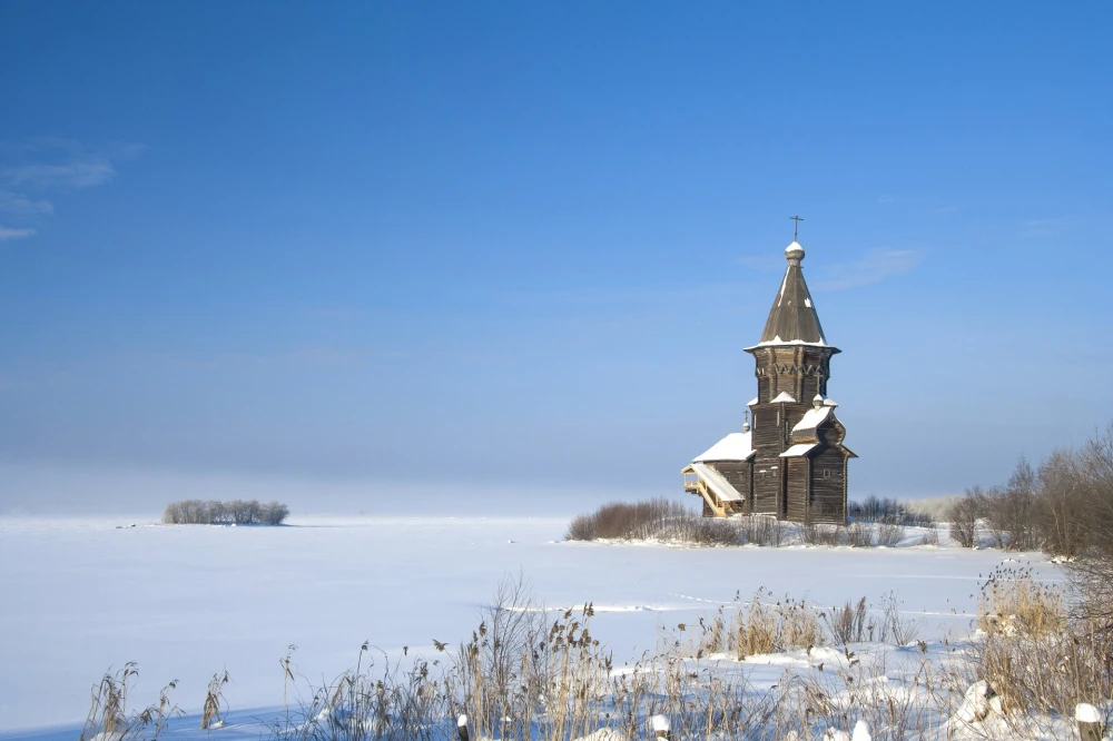 Зимний снежный пейзаж с русской северной деревянной церковью на берегу Онежского озера. Церковь Успения Пресвятой Богородицы в городе Кондопога. Большое пространство для текста. Карелия, Россия